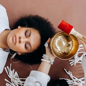 A woman experiencing sound healing therapy with a Tibetan singing bowl indoors